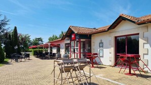 Un patio con mesas y sillas, un edificio con tejado de baldosas y un letrero del restaurante 'ibis'.