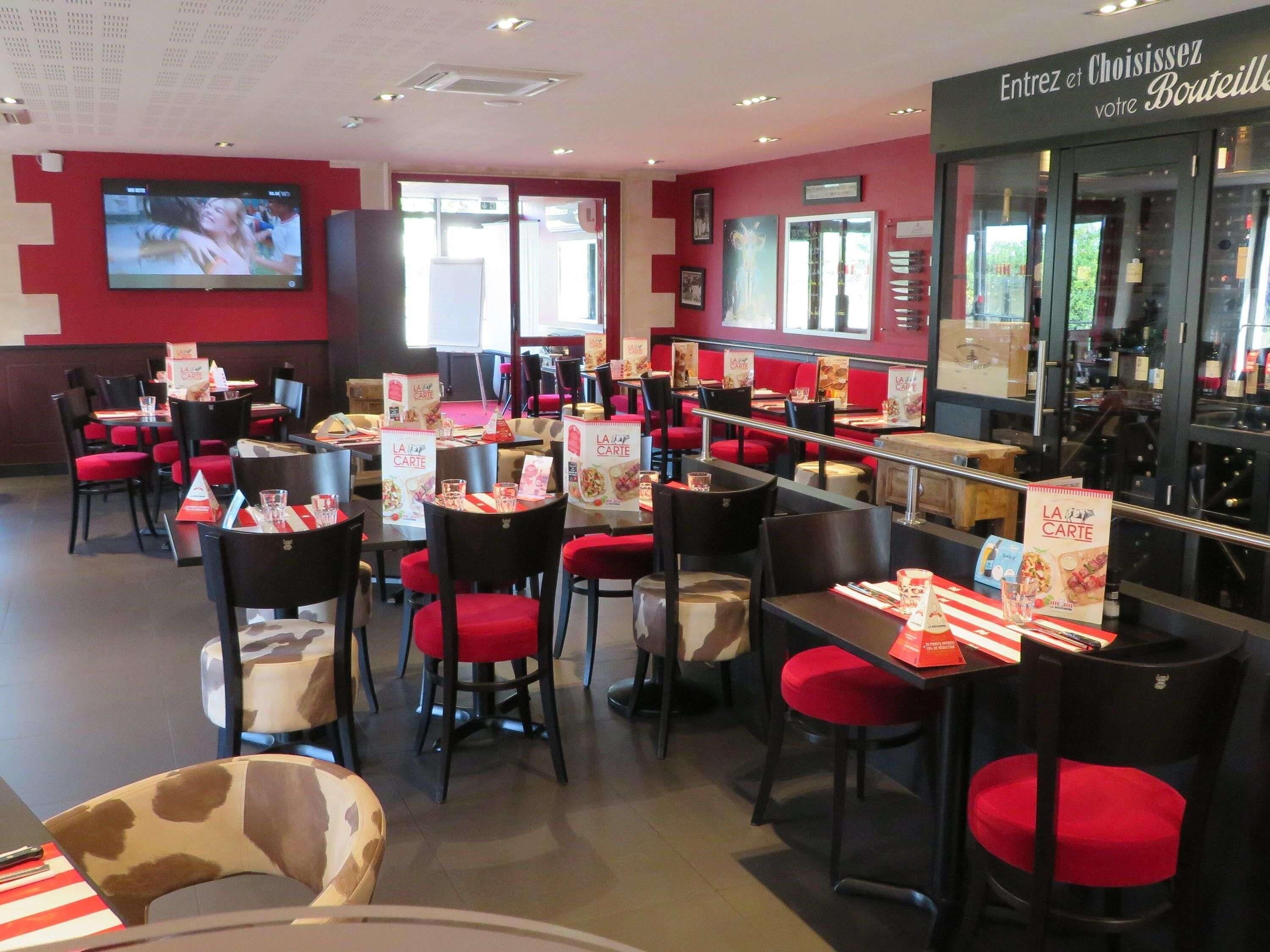 Un interior de restaurante con sillas, mesas y un atril para el menú, todo en rojo.