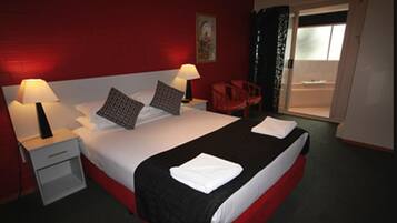 Habitación de hotel con una cama grande, dos mesitas de noche con lámparas, una silla roja y vistas a través de un ventanal.