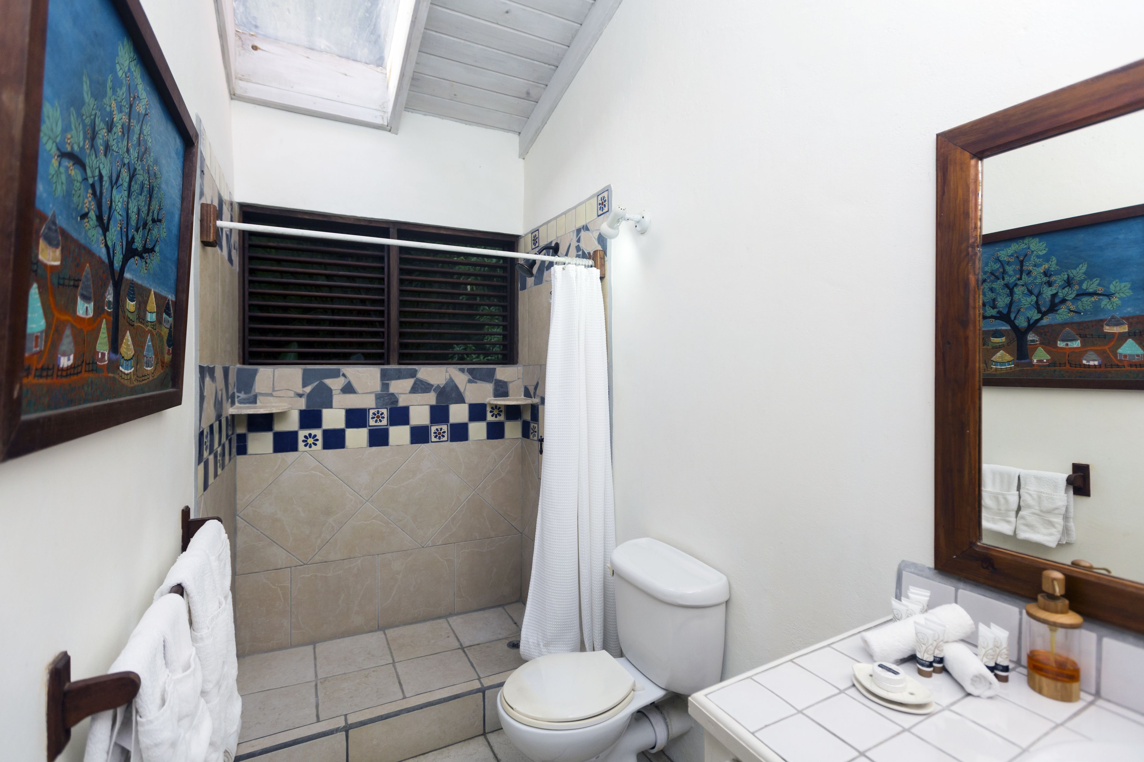 A bathroom with a shower, toilet, and sink. There are towels and toiletries on the sink counter.