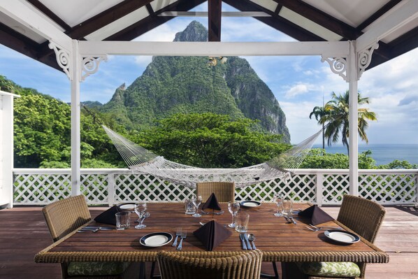 A wooden deck with a table set for dining, overlooking a mountainous landscape with a hammock. - Stonefield Villa Resort (Soufrière)
