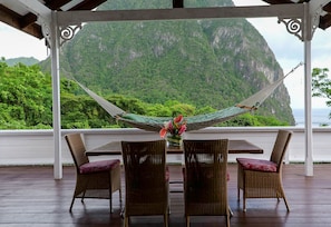 A covered outdoor seating area with wicker chairs and a table, overlooking a mountainous landscape. - Stonefield Villa Resort (Soufrière)