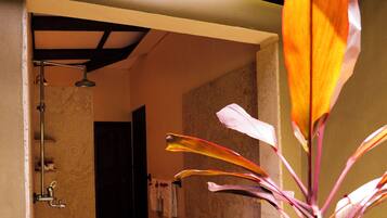 A covered outdoor area with a shower, a tiled floor, and a plant with large leaves.