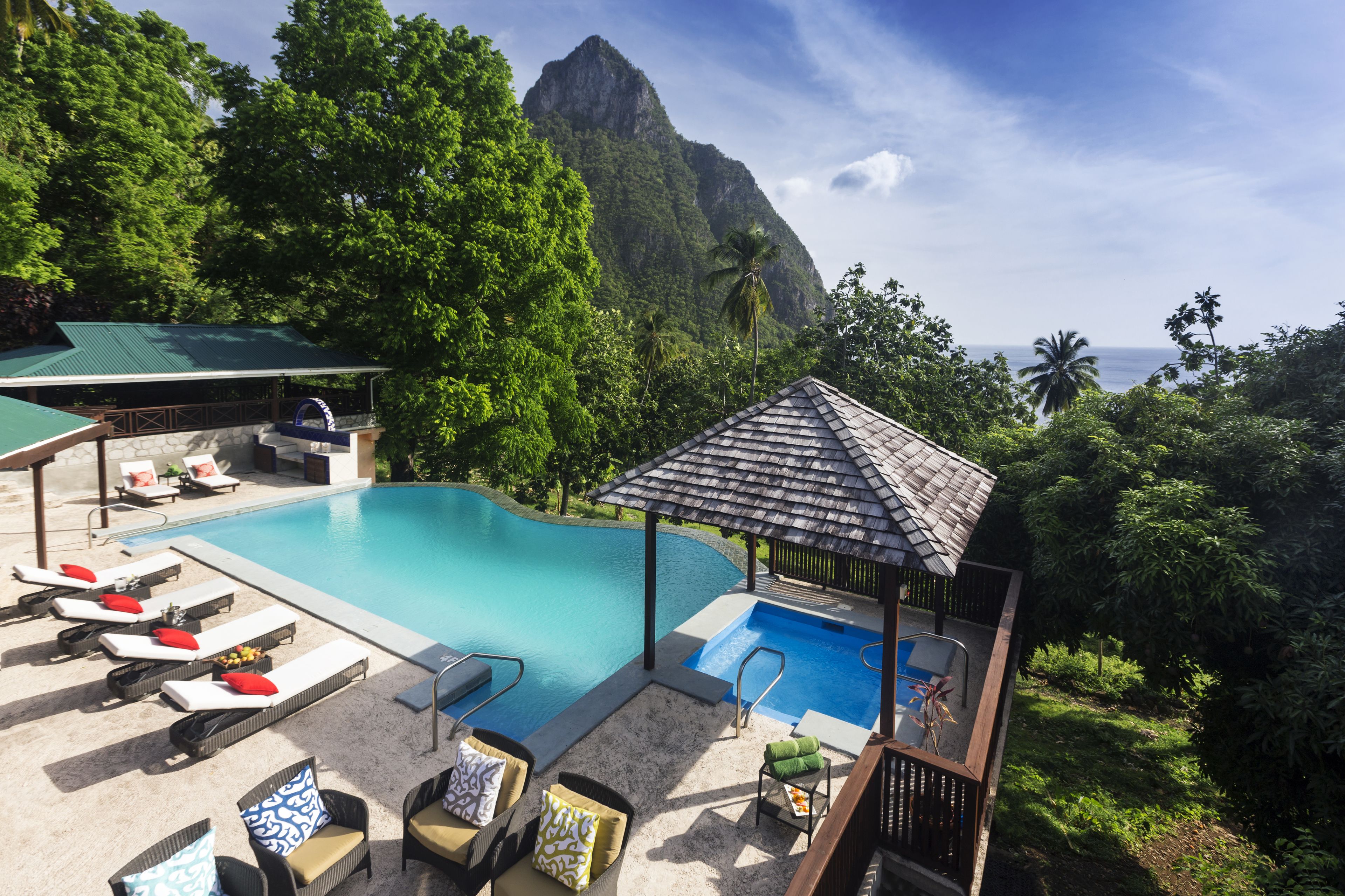 A pool area with lounge chairs and a gazebo, surrounded by lush greenery and a mountain backdrop.