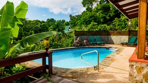 A pool area with a wooden deck, lounge chairs, and a stone wall. - Stonefield Villa Resort (Soufrière)