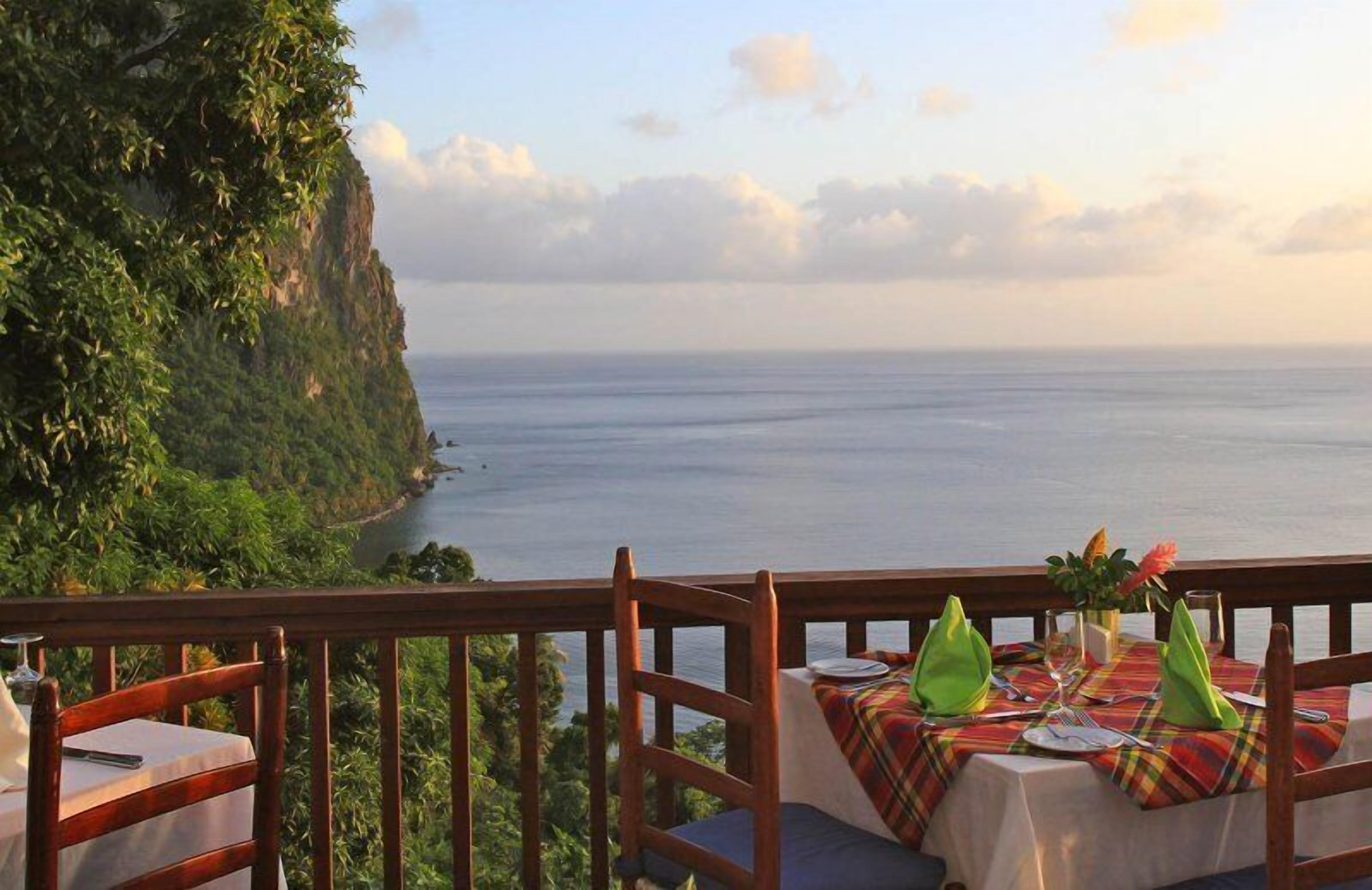 A table set for dining with a view of the ocean and a cliff.
