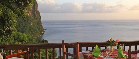 A table set for dining with a view of the ocean and a cliff.
