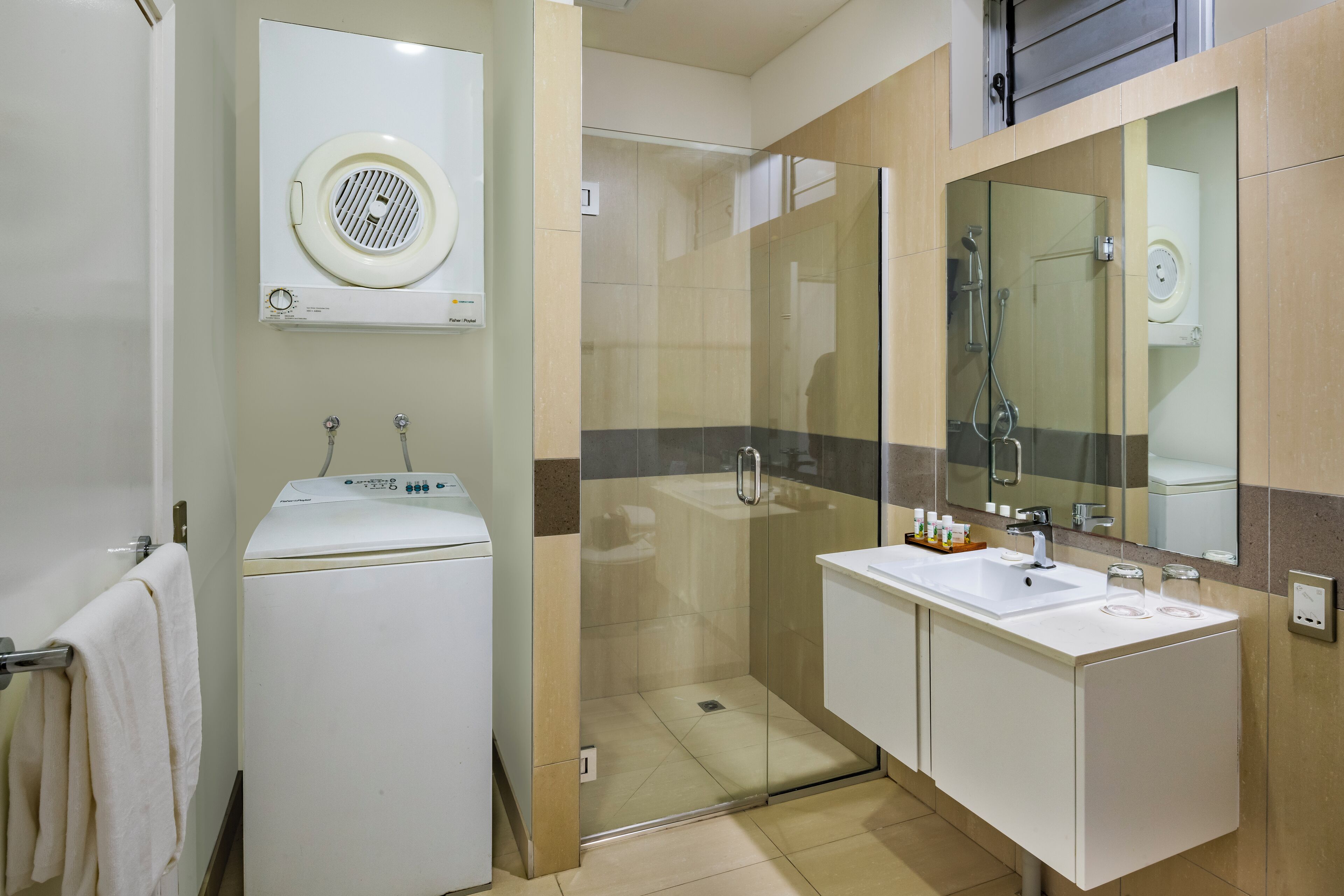 A modern bathroom with a glass-enclosed shower, a built-in washing machine, and a large mirror above the sink.