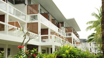 A multi-story hotel with balconies, a garden area with tropical plants, and a clear sky.