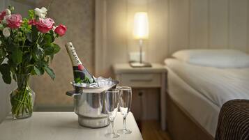 A hotel room with a bed, a bedside table with a lamp, a vase of flowers, a champagne bottle in a bucket, and two glasses.