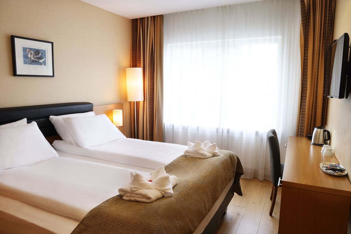 A hotel room with two beds, a desk, a chair, a lamp, and a framed picture on the wall.