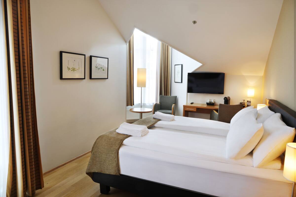 A hotel room with a large bed, a desk, a chair, a TV, and framed pictures on the wall.