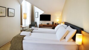 Habitación de hotel con cama, escritorio, silla, televisión y ventana con cortinas.