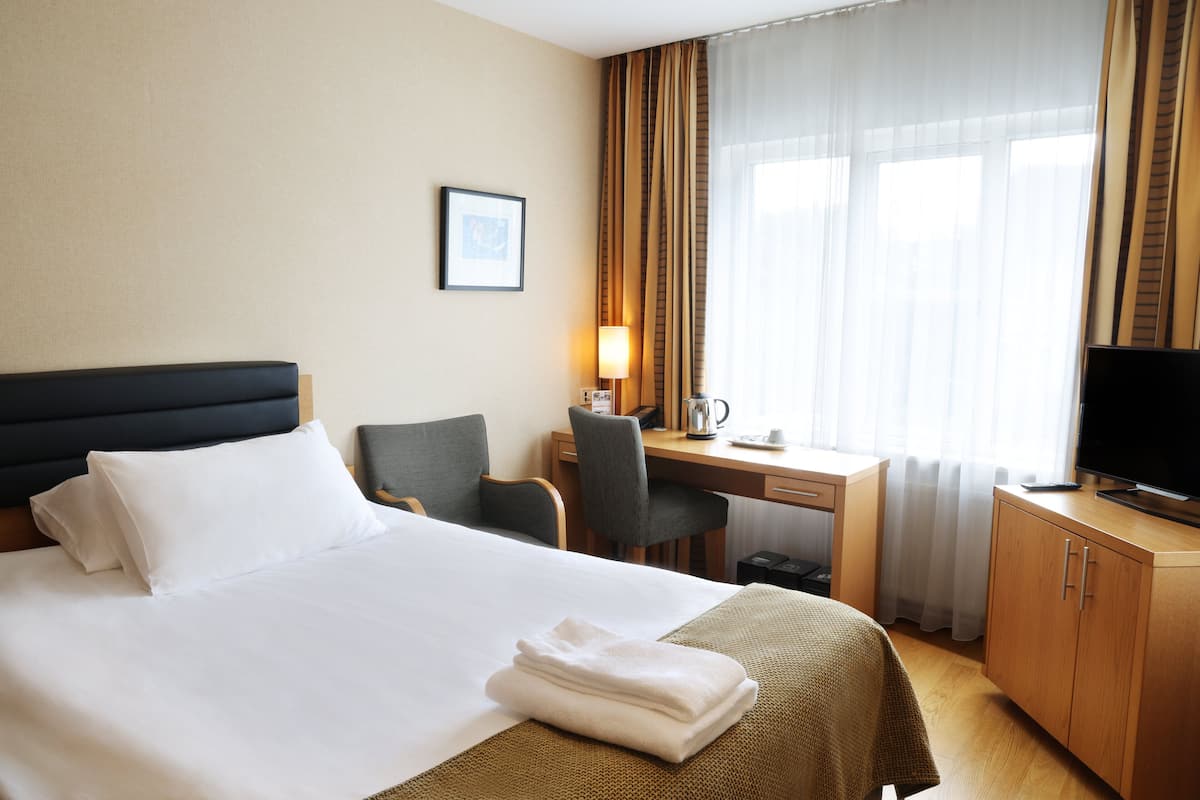 A hotel room with a bed, a desk, a chair, a television, and a window with curtains.