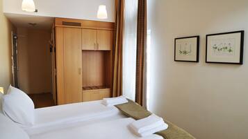 A hotel room with a bed, a wardrobe, a shower, and two framed botanical prints on the wall.