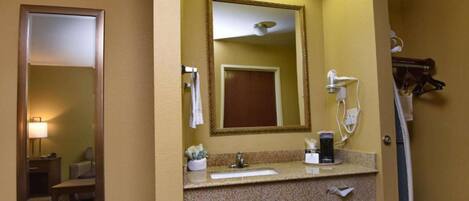 A hotel bathroom with a large mirror, a sink, and a shower area.
