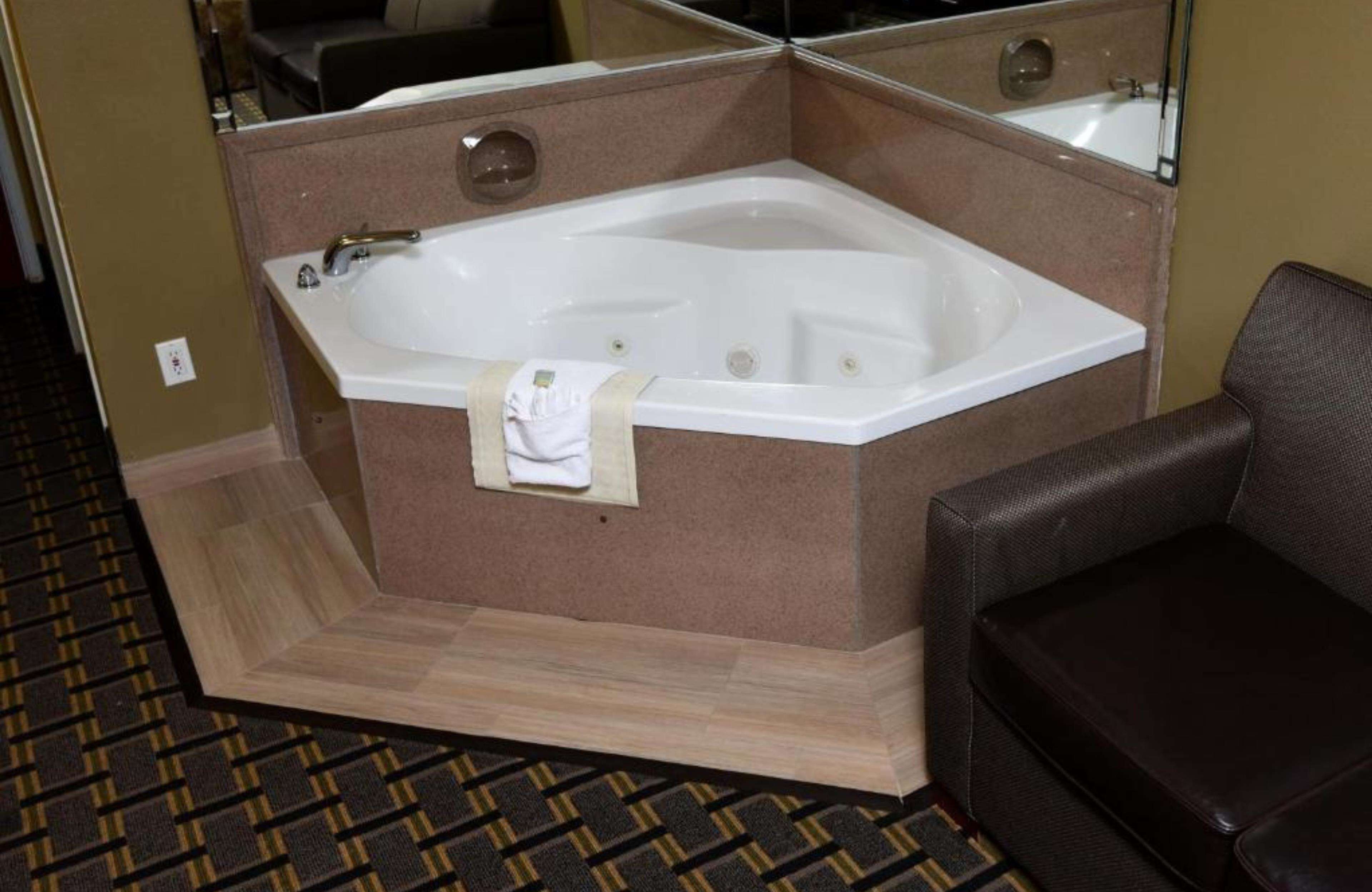 Ein Hotelzimmer mit einer großen Badewanne, einem dunkelbraunen Ledersessel und einem gemusterten Teppich.