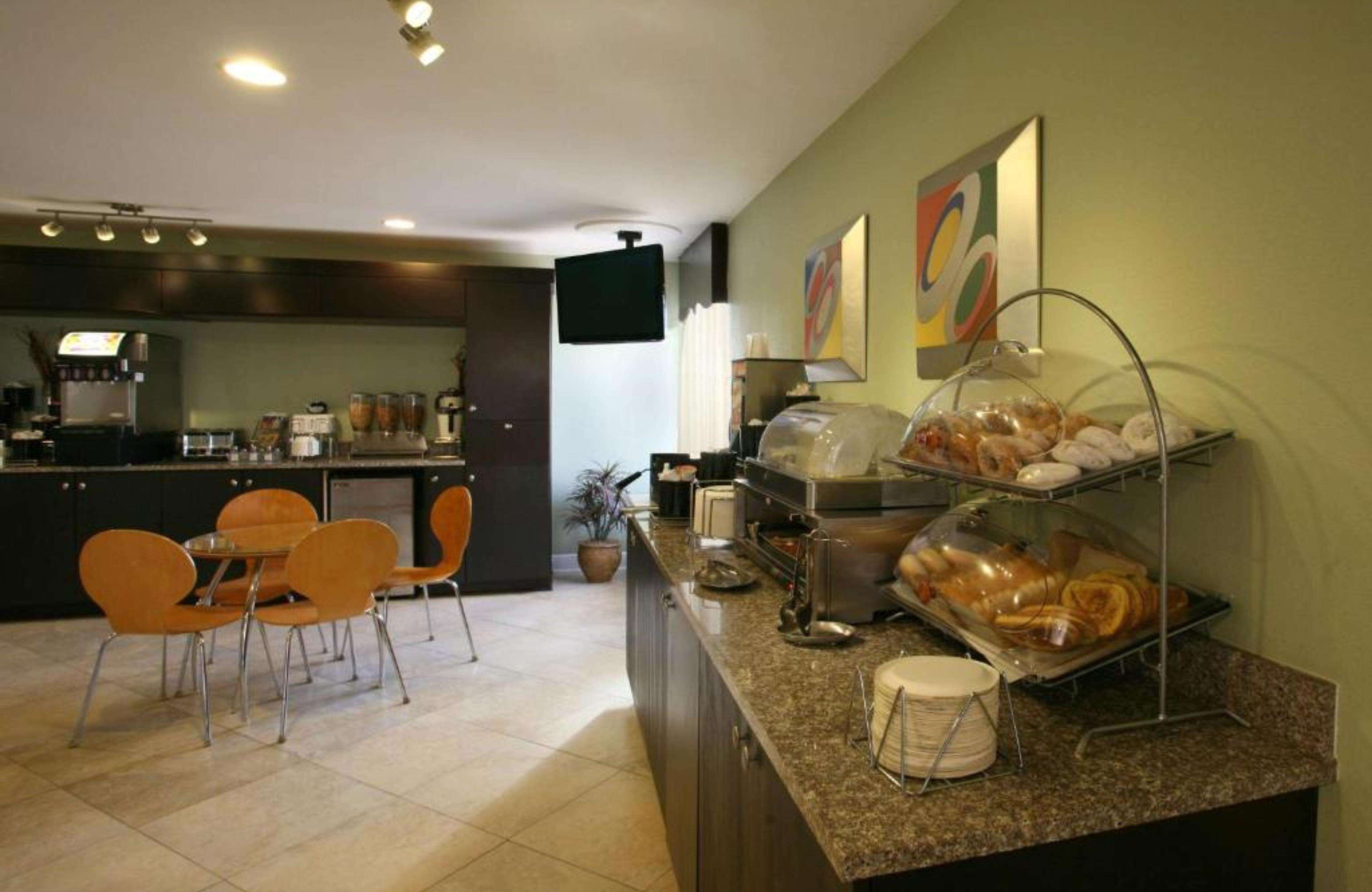 A hotel breakfast area with a counter, seating, and a TV.