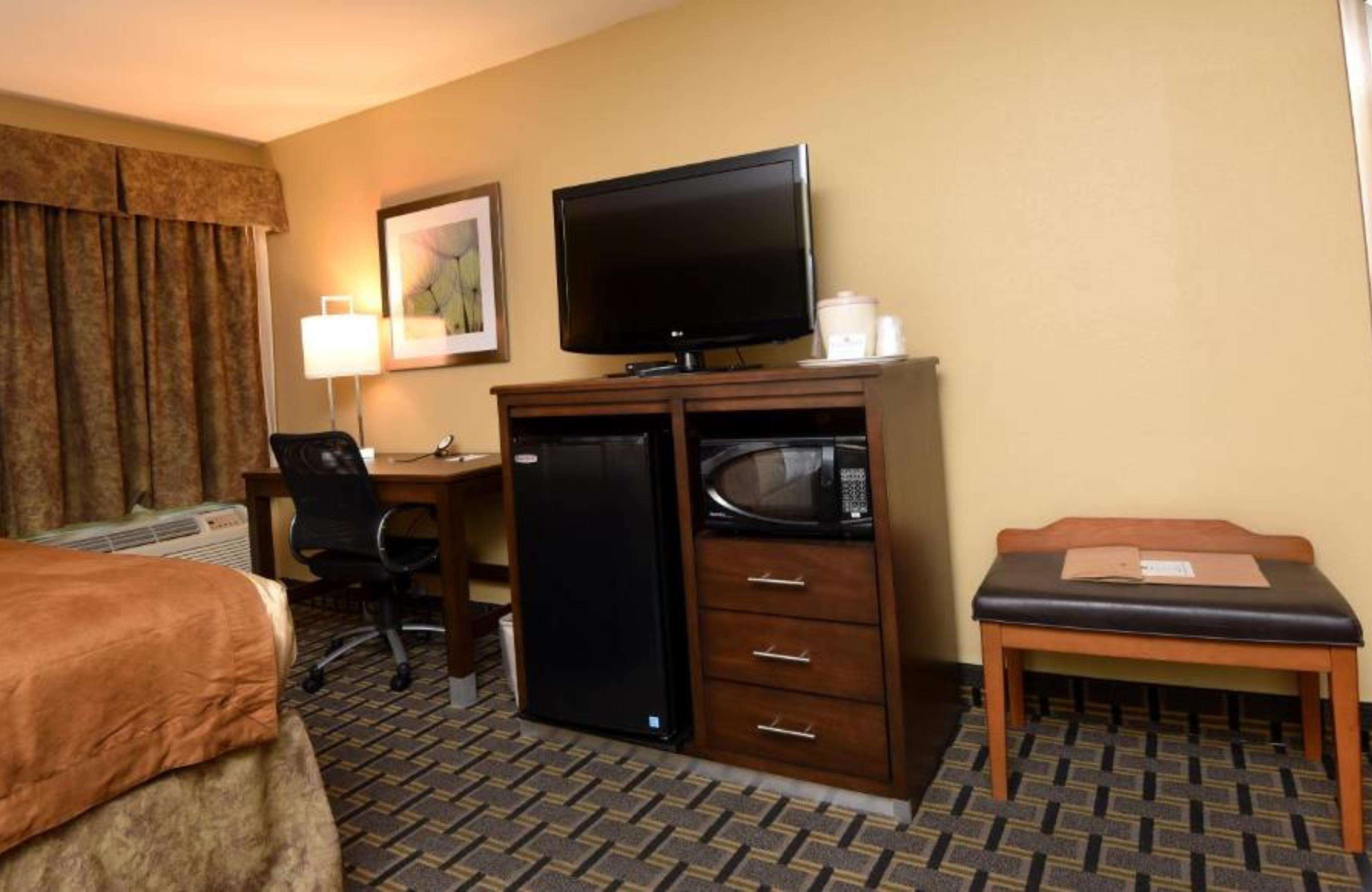 Une chambre d’hôtel comprenant un lit, un bureau avec un ordinateur, une tél évision, un réfrigérateur, un four à micro-ondes et une petite table.