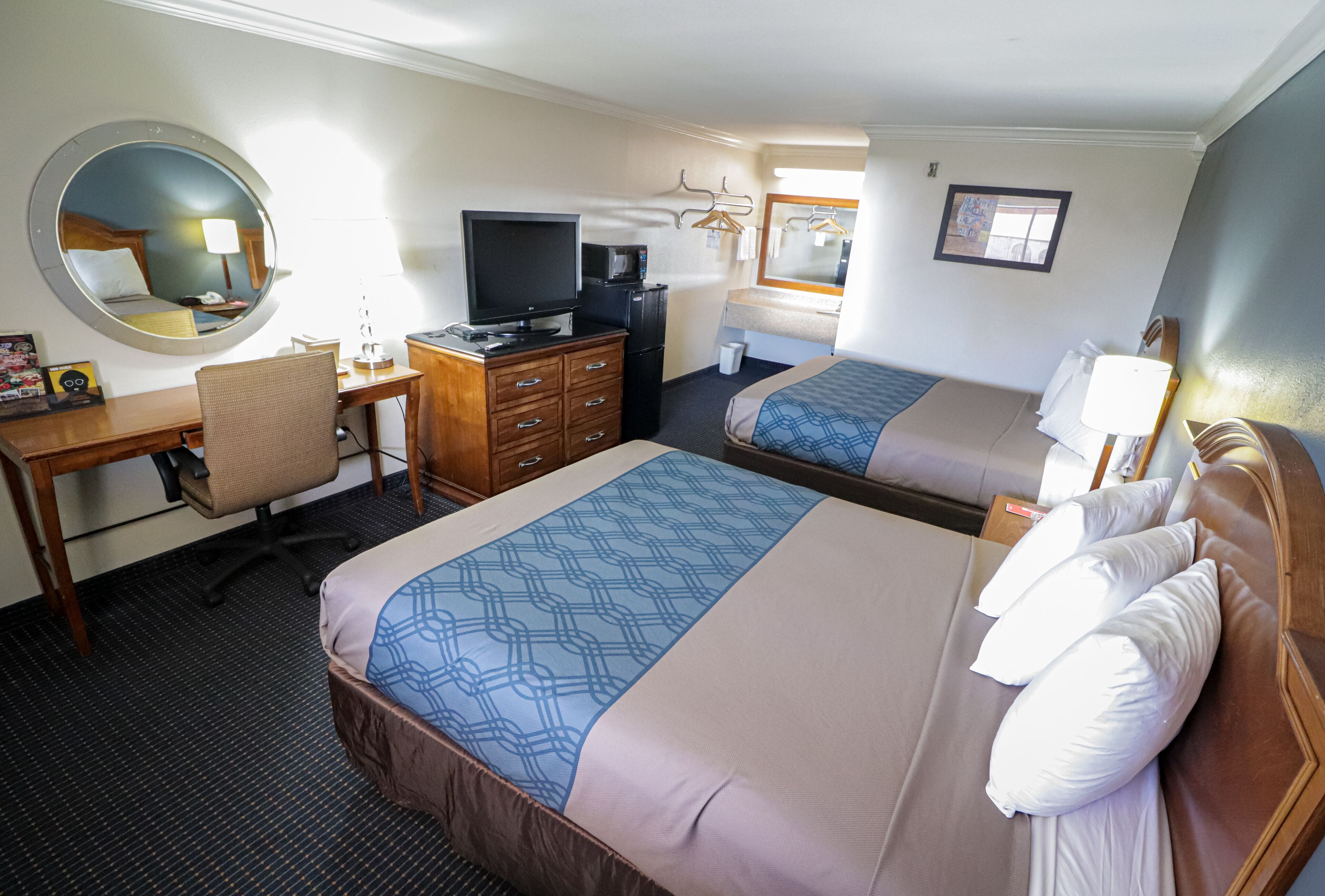 A hotel room with two beds, a desk with a computer, a TV, and a mirror.