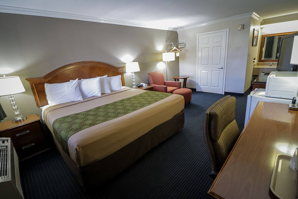 Una habitación de hotel con una cama grande, un escritorio, una silla, una lámpara de escritorio, una mesita de noche, un espejo y una puerta.
