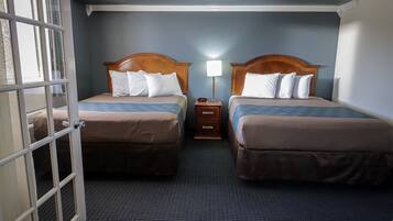 A hotel room with two beds, a nightstand, and a window with curtains.