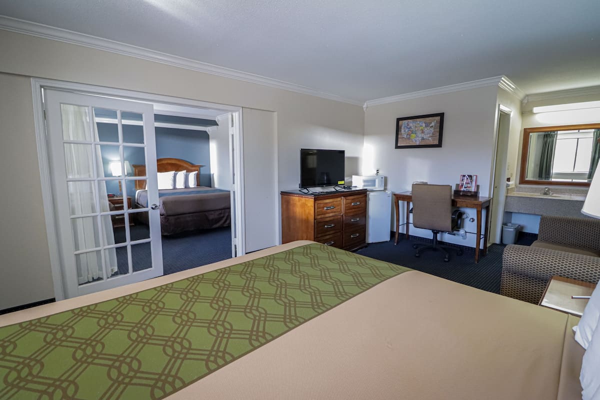 Habitación de hotel con cama, escritorio, silla, televisión y espejo de baño.