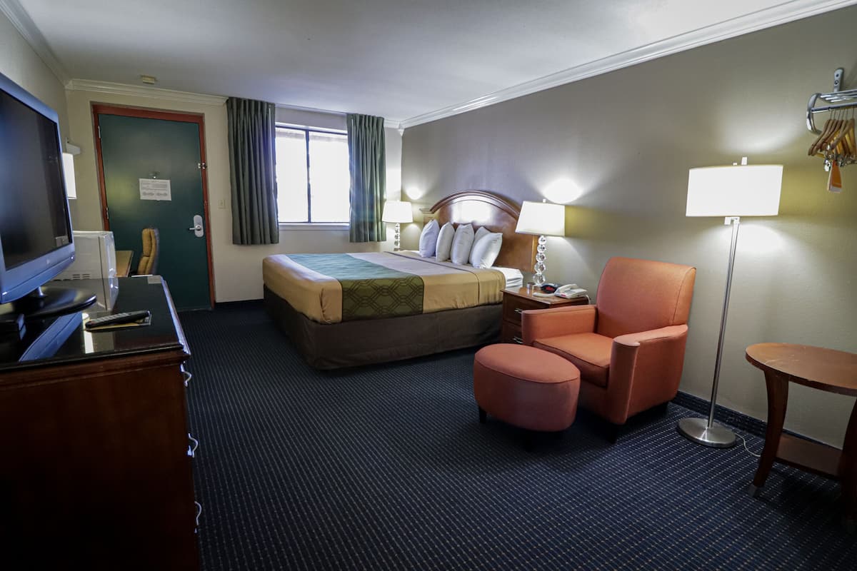 Una habitación de hotel con cama, escritorio con televisor, silla, mesa y lámpara de pie.