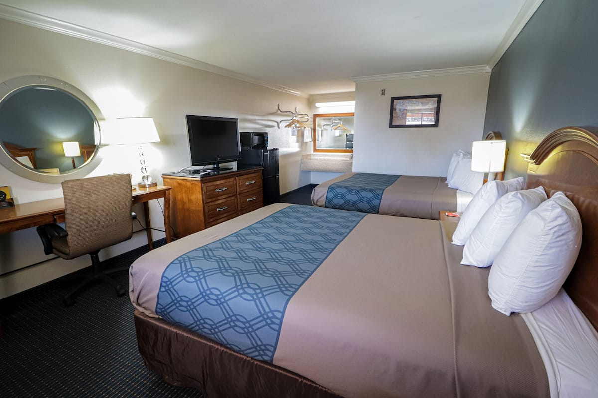 Habitación de hotel con dos camas, un escritorio con computadora, televisor y espejo.