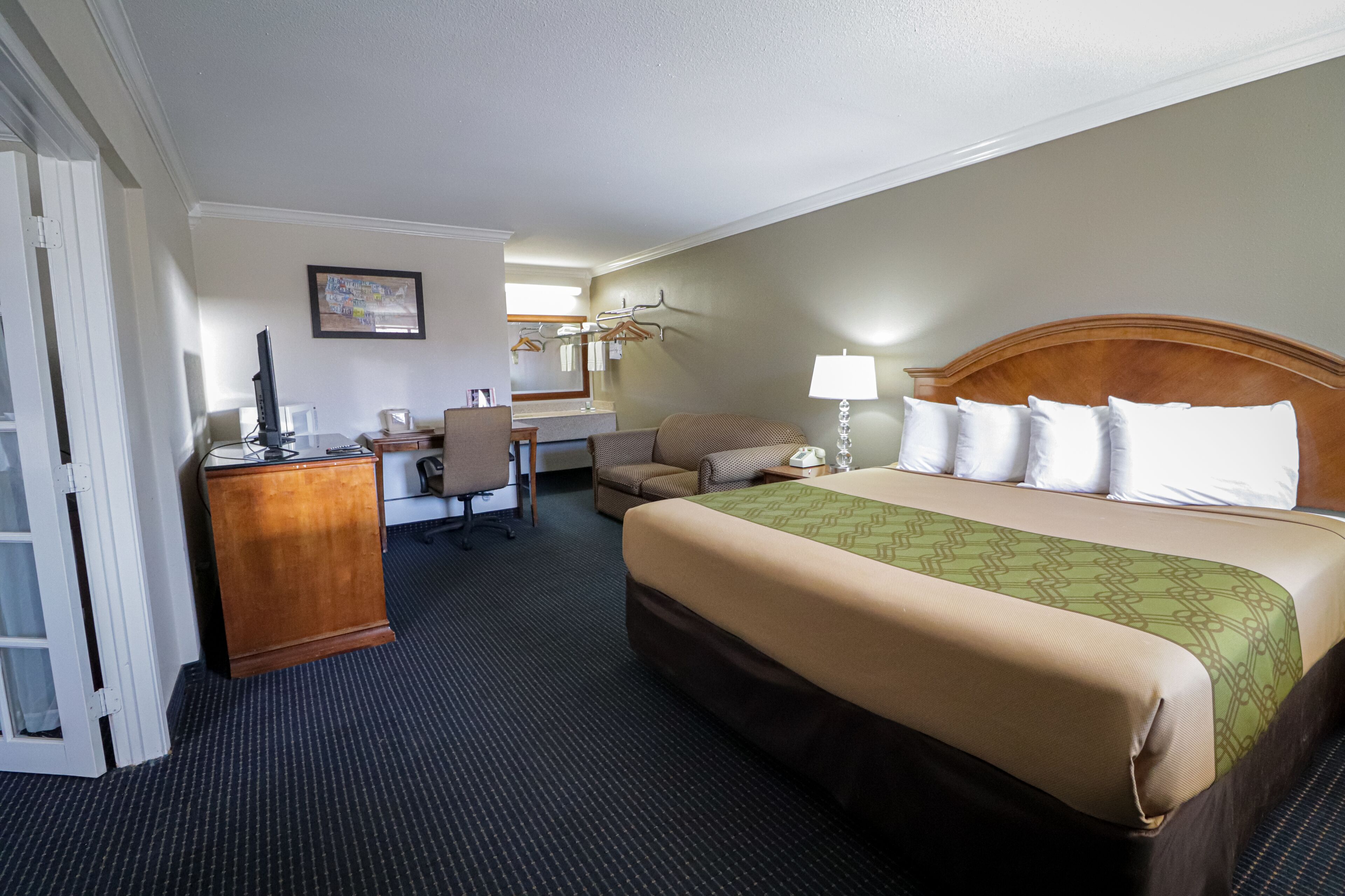 A hotel room with a bed, a desk, a chair, a lamp, and a dresser.