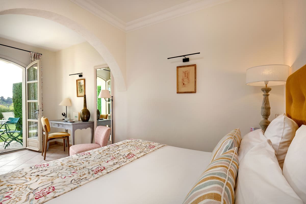A bedroom with a large bed, a desk, a chair, and a view through an open door.