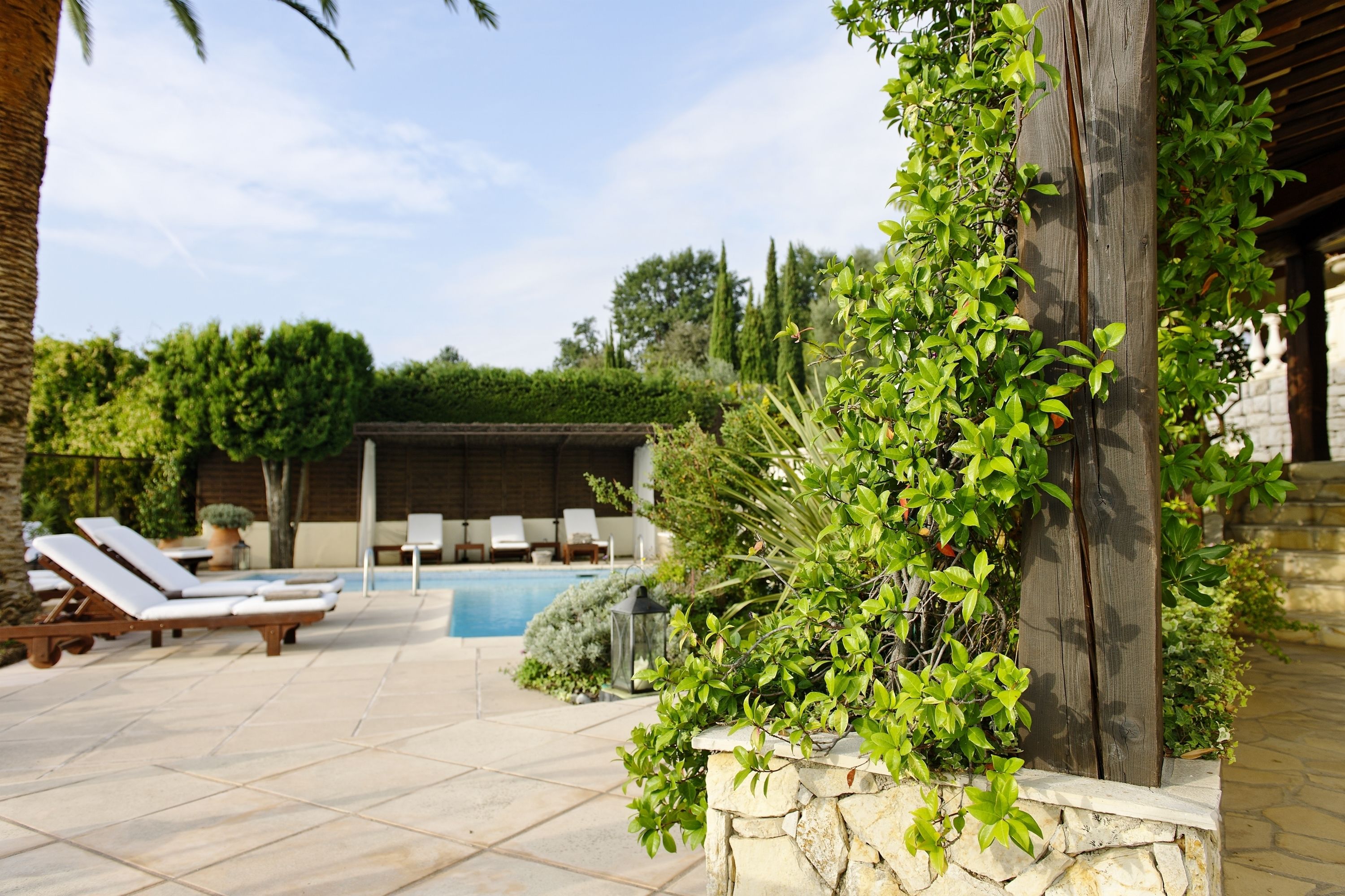 A poolside area with lounge chairs, a stone wall planter with greenery, and a clear view of the pool.