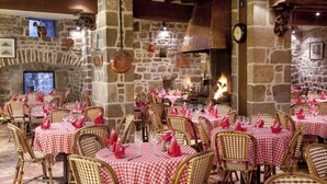 A restaurant with stone walls, wooden beams, and red and white checkered tablecloths. Tables are set with wicker chairs and red napkins. - Auberge Saint-Pierre (Le Mont-Saint-Michel)