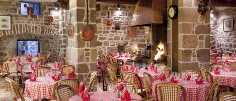 Ein Restaurant mit Steinwänden, Holzbalken und rot-weißen karierten Tischdecken. Die Tische sind mit Korbstühlen und roten Servietten gedeckt.