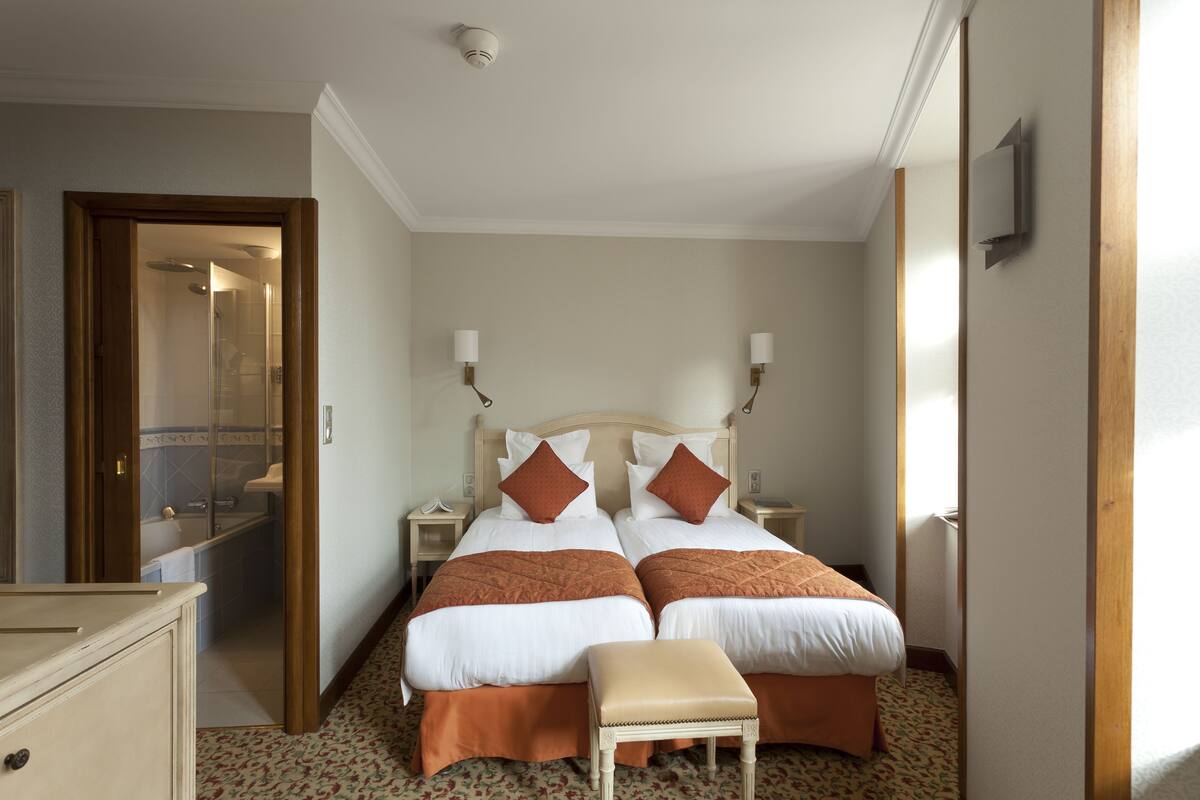 Hotelkamer met twee bedden, een houten bankje, een dressoir en een badkamer die door een open deur zichtbaar is.