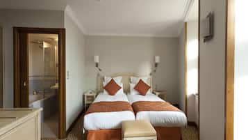 A hotel room with two beds, a wooden bench, a dresser, and a bathroom visible through an open door.