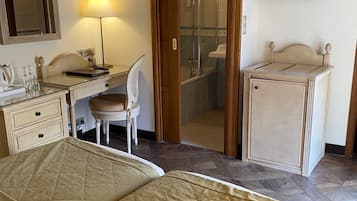 A hotel room with a bed, a desk, a chair, a TV, and a bathroom visible through an open door.
