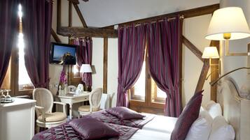 A hotel room with a bed, two chairs, a desk, a television, and curtains.