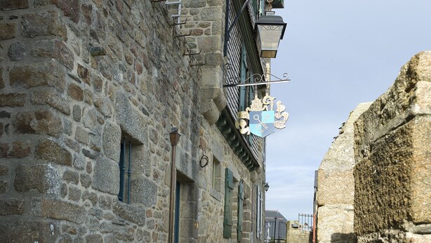 A narrow stone-paved street flanked by historic stone buildings with traditional shutters and a metal balcony railing. - Auberge Saint-Pierre (Le Mont-Saint-Michel)