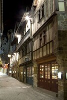 Una calle histórica con edificios de piedra, contraventanas de madera y letreros iluminados.