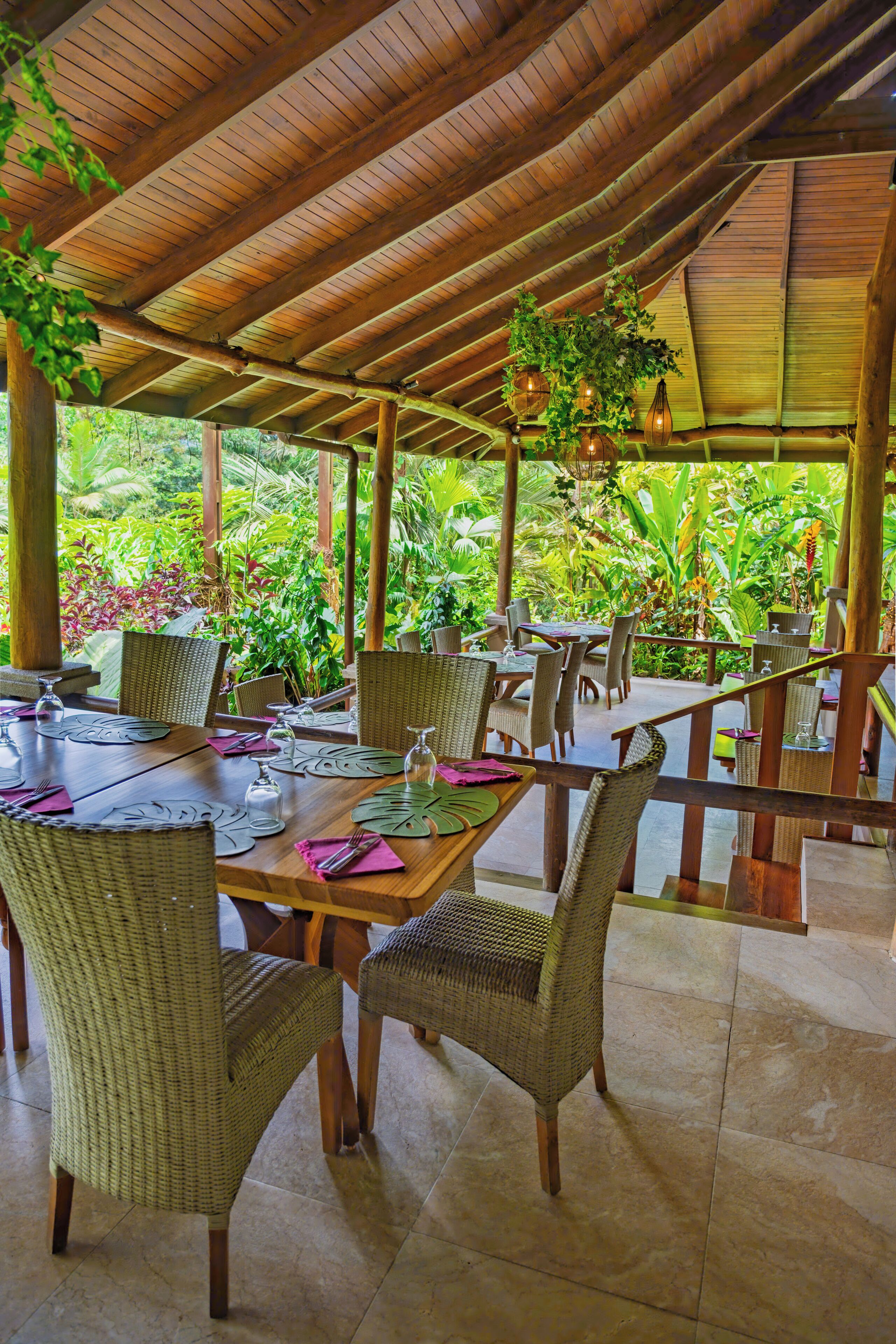 A covered outdoor dining area with wicker furniture and hanging plants.