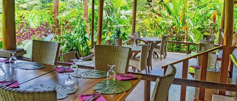 A covered outdoor dining area with wicker furniture and hanging plants.