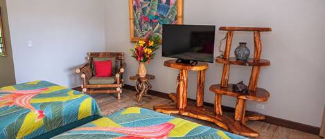 A room with two beds, a television on a wooden stand, a chair, and a decorative vase with flowers.