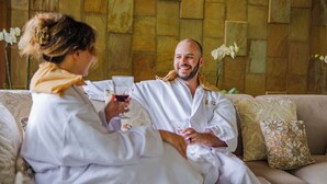 A couple sitting on a beige sofa with patterned cushions, holding wine glasses. - Lost Iguana Resort and Spa (La Fortuna)