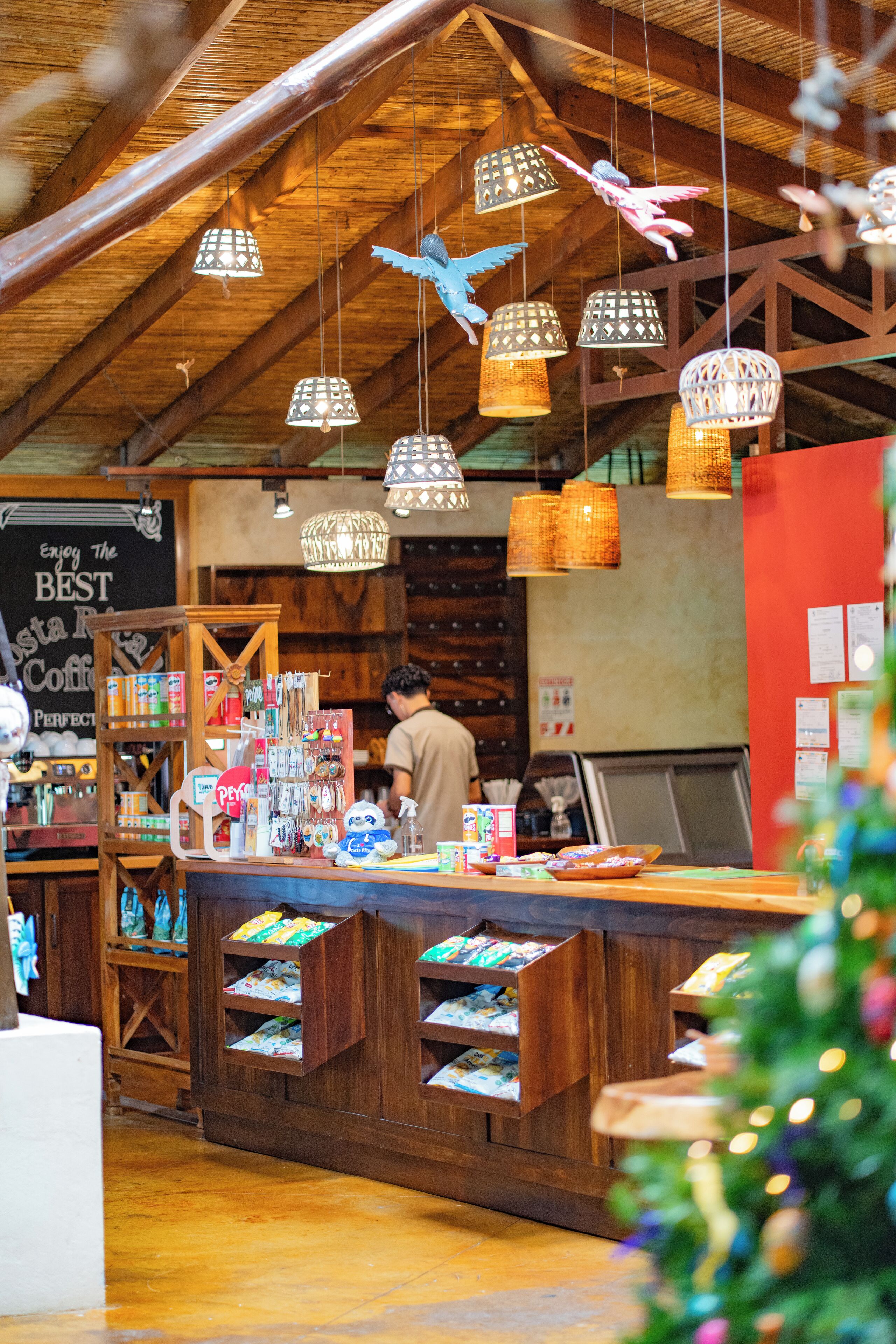 A rustic interior with wooden beams, hanging wicker lamps, and a counter displaying various items.
