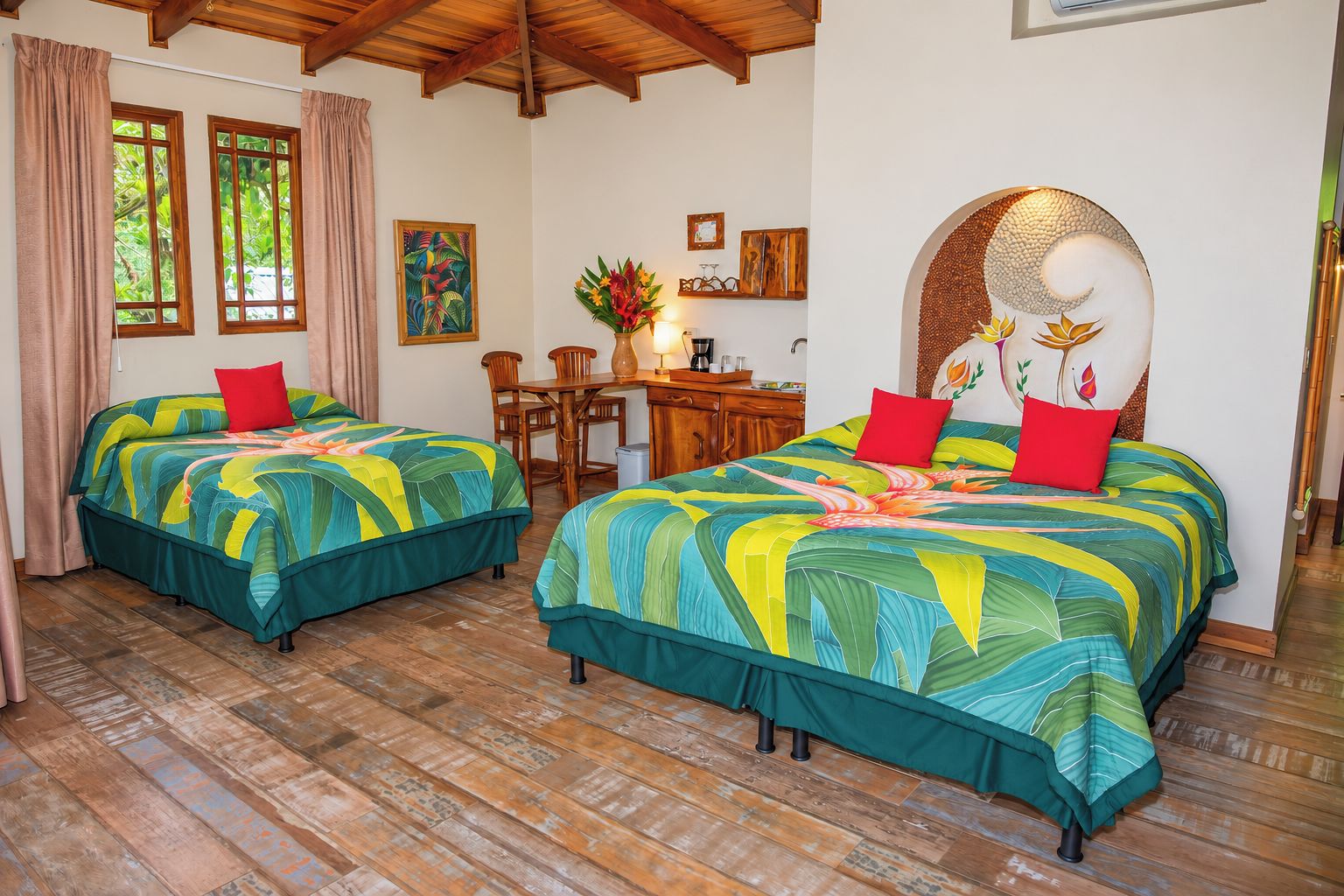 A hotel room with two beds, a wooden ceiling, a desk with a chair, and a window with curtains.