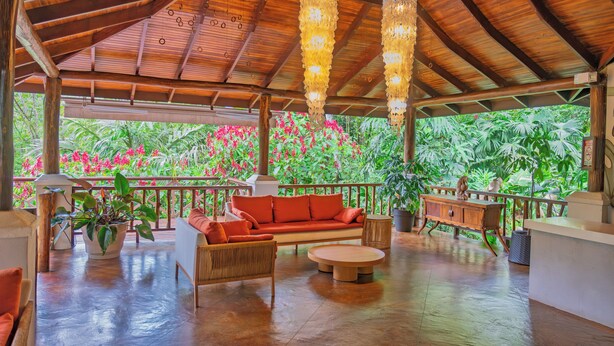 A covered outdoor seating area with a wooden bench, a sofa, and a round table. - Lost Iguana Resort and Spa (La Fortuna)