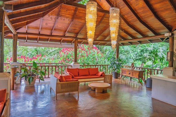 A covered outdoor seating area with a wooden bench, a sofa, and a round table. - Lost Iguana Resort and Spa (La Fortuna)
