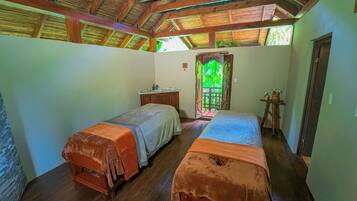 A room with two beds, a wooden ceiling, a small table, and a door leading to a balcony.