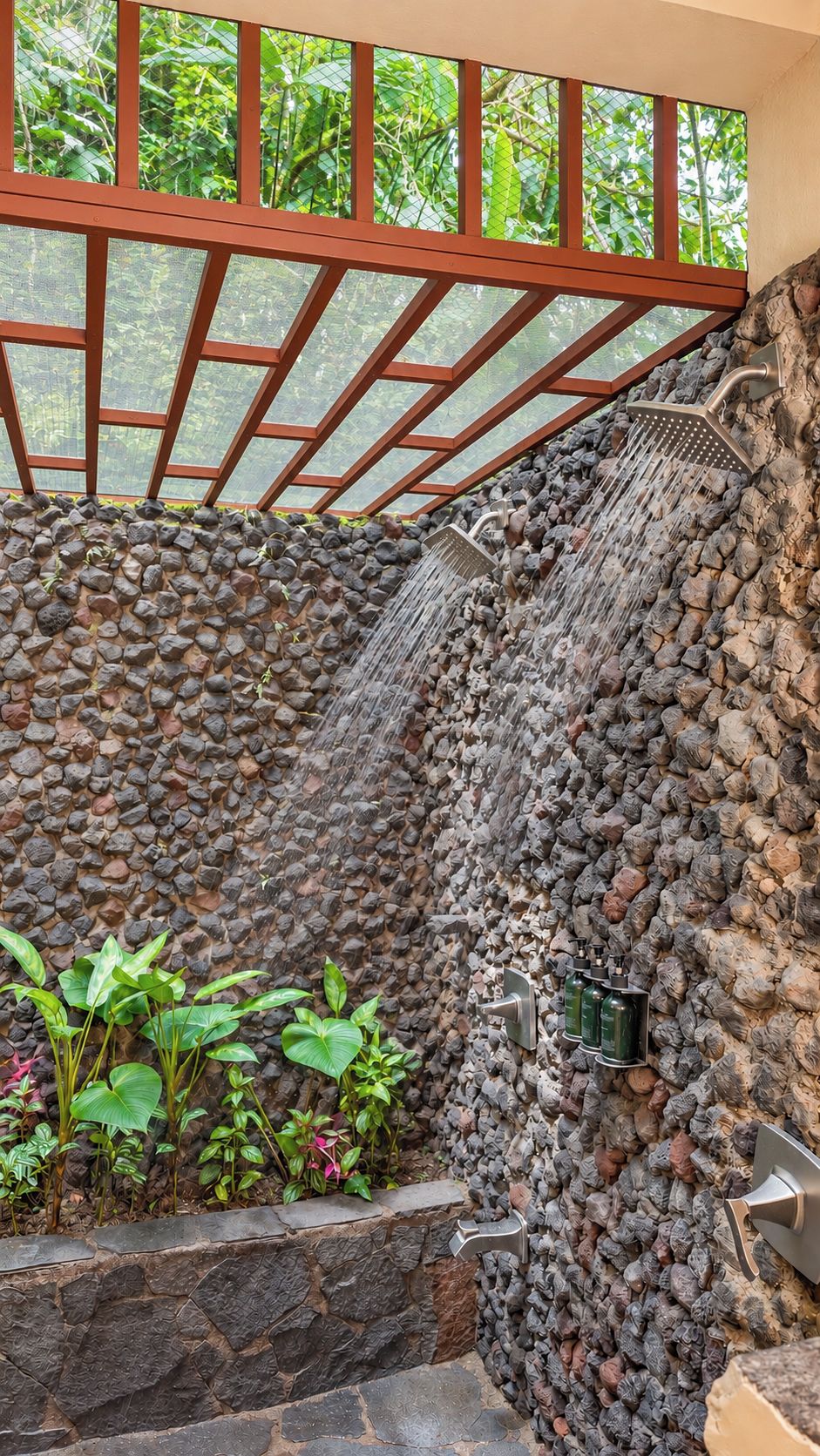 Una fuente de piedra con cascada, rodeada de plantas y una barandilla de metal.